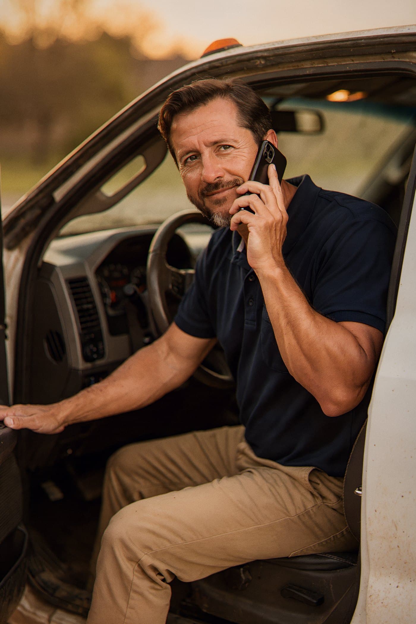 A contractor taking a call from the driver's seat of his truck in the morning light.