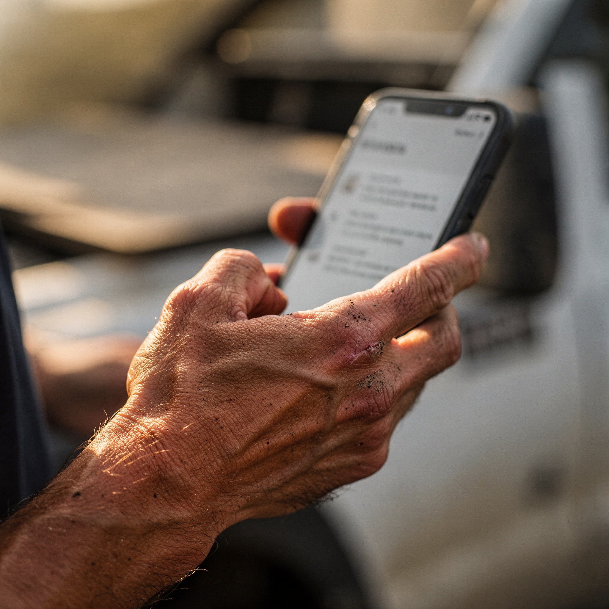 A close-up of a work-worn hand holding a phone showing a price list, in the cab of a work truck.
