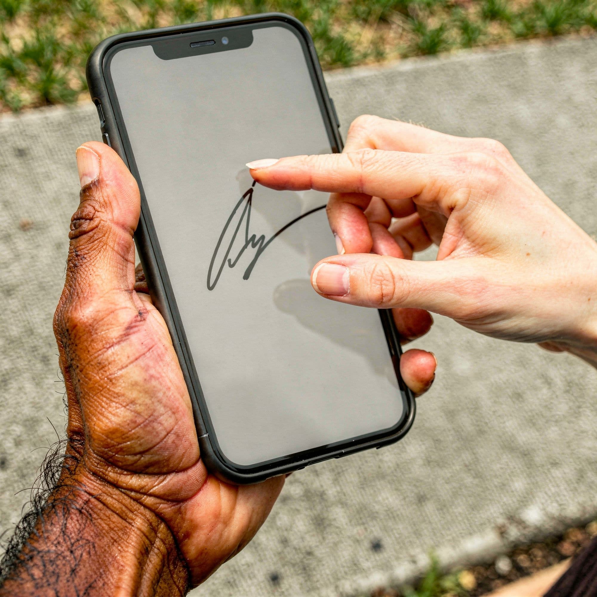 A customer's finger drawing a signature on a phone held steady in a contractor's weathered hand, on a sunlit front walk.